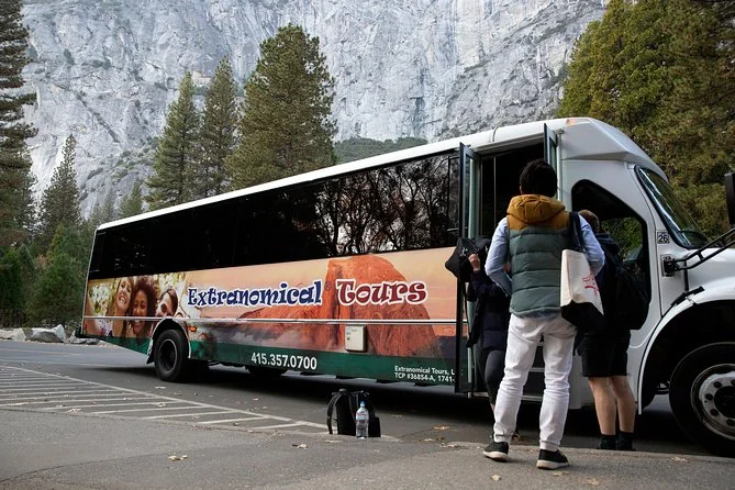Travellers boarding a tour minibus in Yosemite Valley below a granite cliff