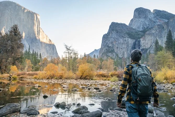 A hiker with a backpack by the Merced River in autumn, El Capitan behind